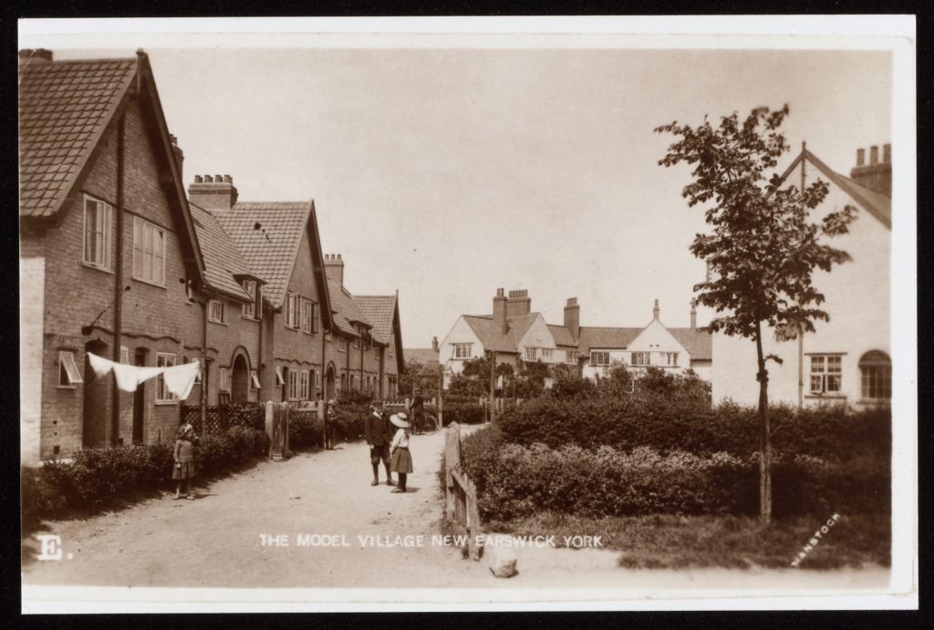 Black and white postcard showing New Earswick village, image shows cottage style houses with washing hanging outside.